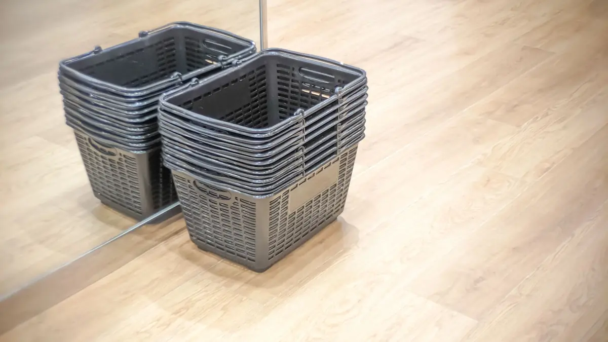 Two stacks of empty grey shopping baskets on a wooden shop floor beside a mirror
