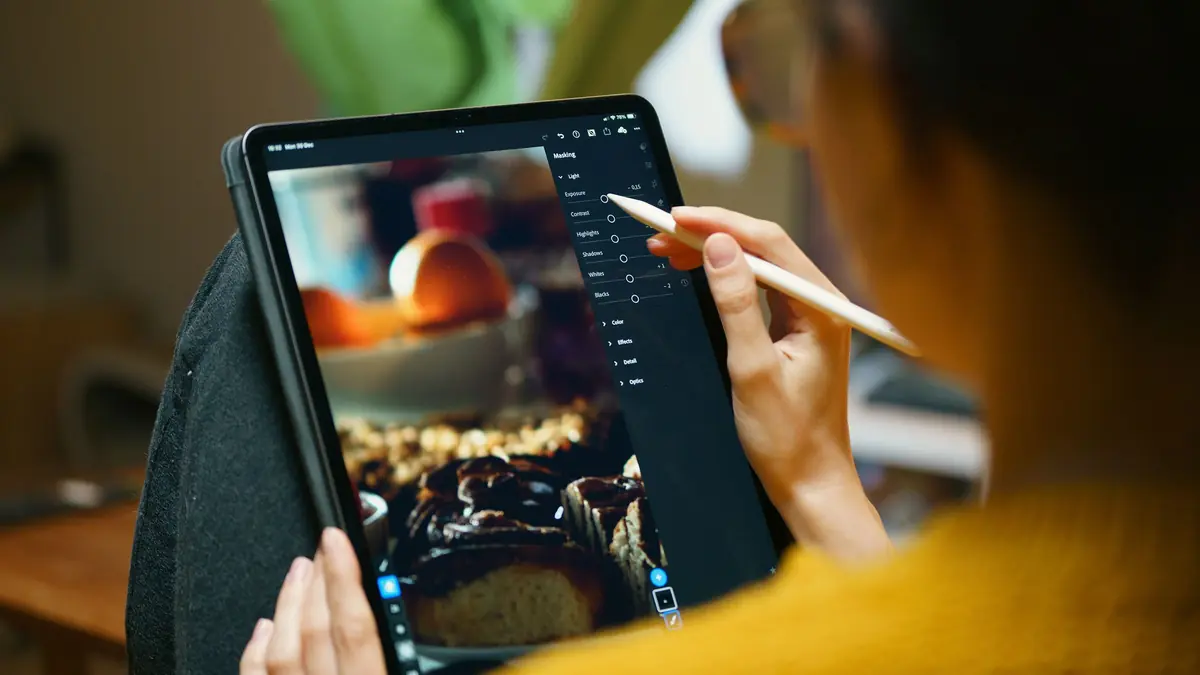 A woman edits a photo of baked goods on a tablet with a stylus