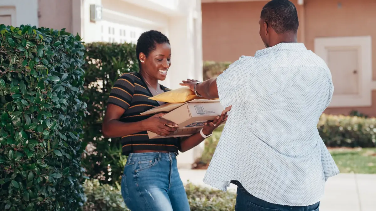 A smiling woman takes a stack of parcels from a delivery man outside a house