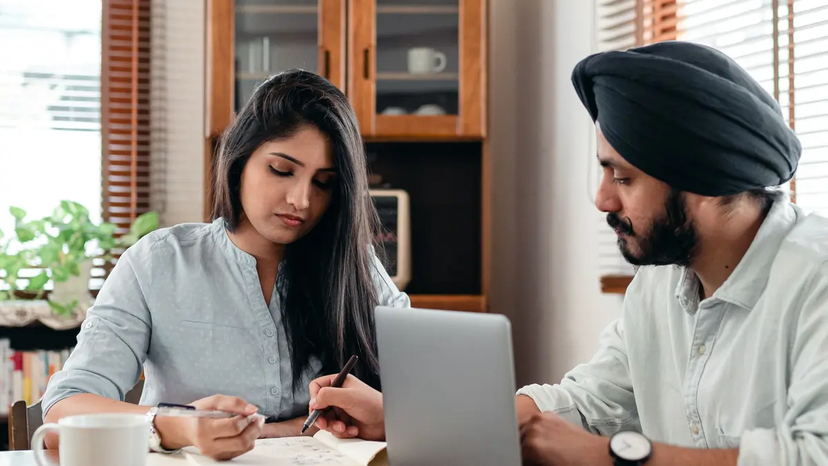 A woman and a man in a turban go through papers together at a table with a laptop