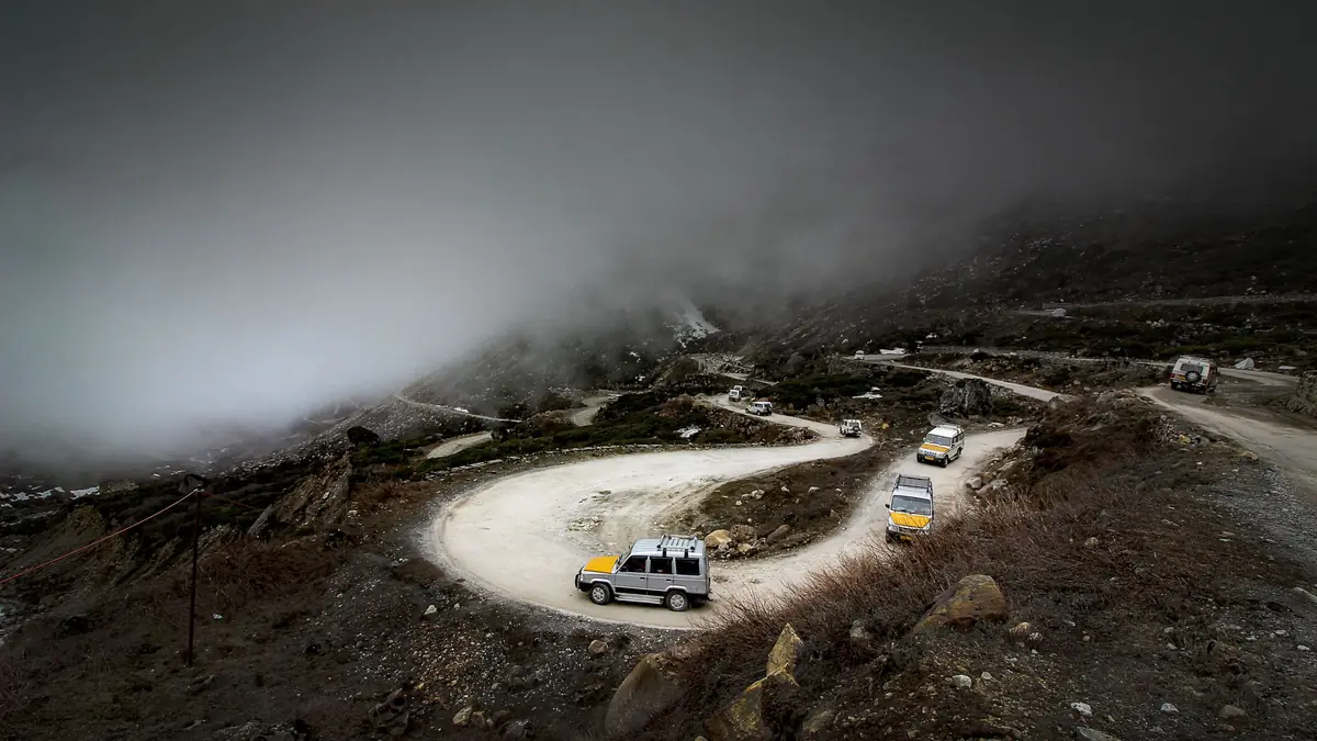 Vehicles wind along a misty mountain road with hairpin bends in Sikkim
