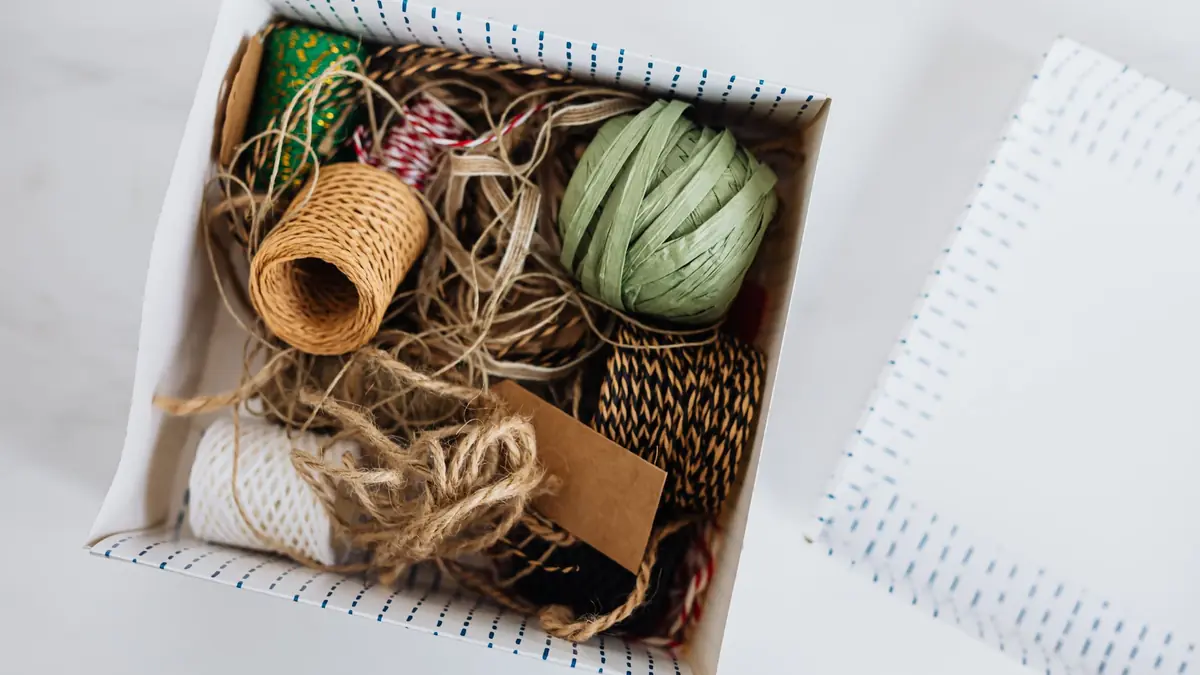 Top view of a gift box filled with rolls of jute twine, paper raffia and string, with a blank kraft tag