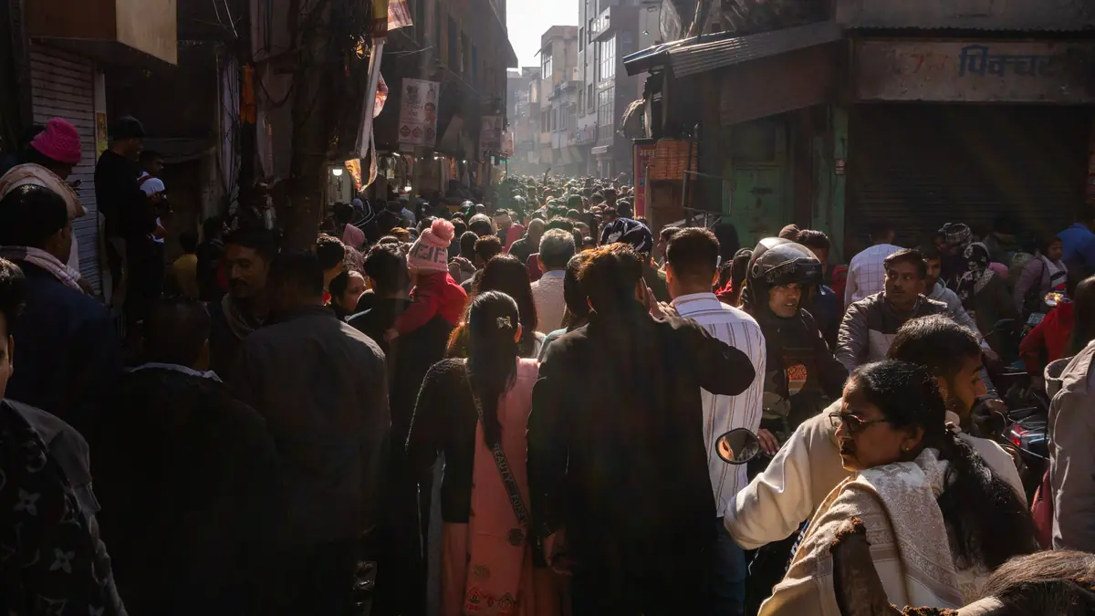 A dense crowd of shoppers fills a narrow market street lined with shops in India