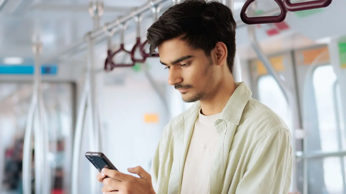 A young man looks down at his smartphone while standing in a metro train carriage