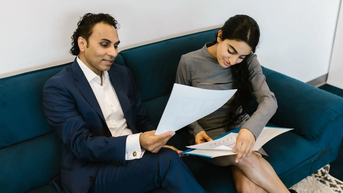 A man and a woman sit on a sofa going through printed documents together