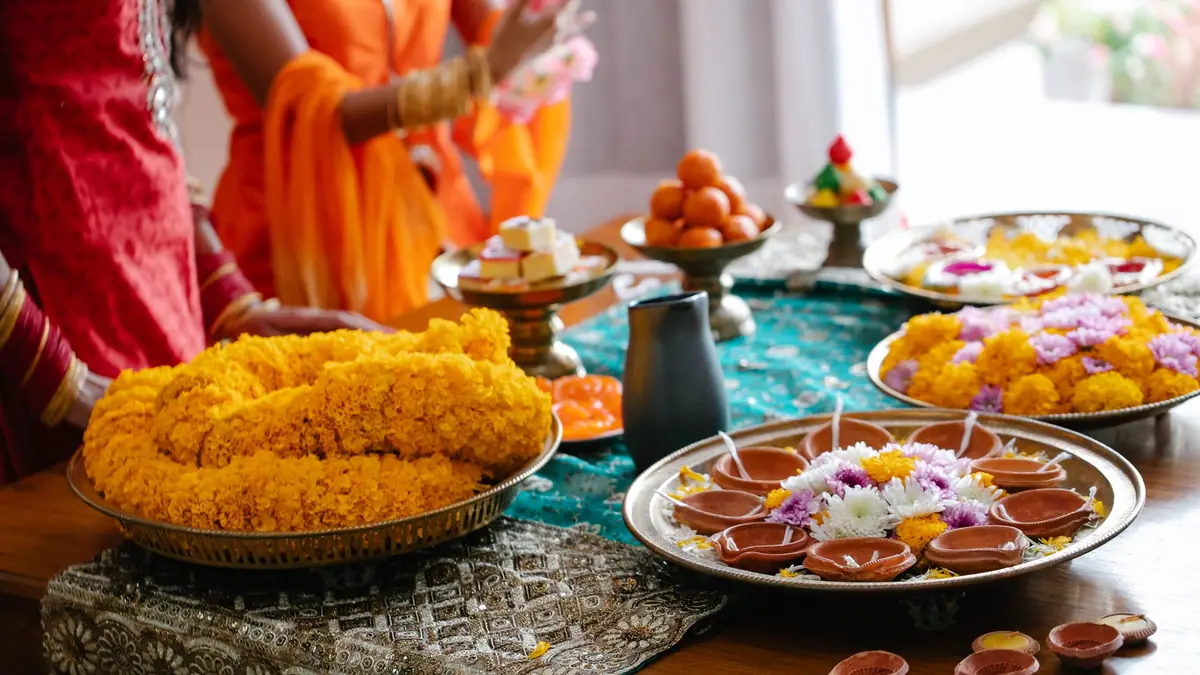 A festive table with marigold garlands, clay diyas, flower petals and sweets on brass plates