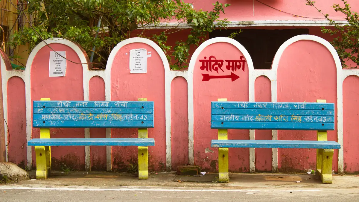 Two blue benches against a pink arched wall, with a Hindi sign pointing to Mandir Marg