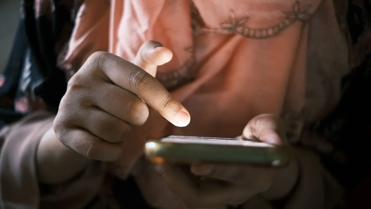 A close-up of a finger about to tap the screen of a smartphone held in one hand