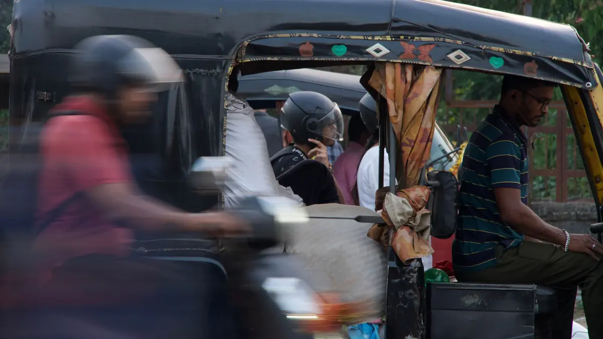 Passengers ride in a black auto-rickshaw as a motorbike passes in a blur on a city street
