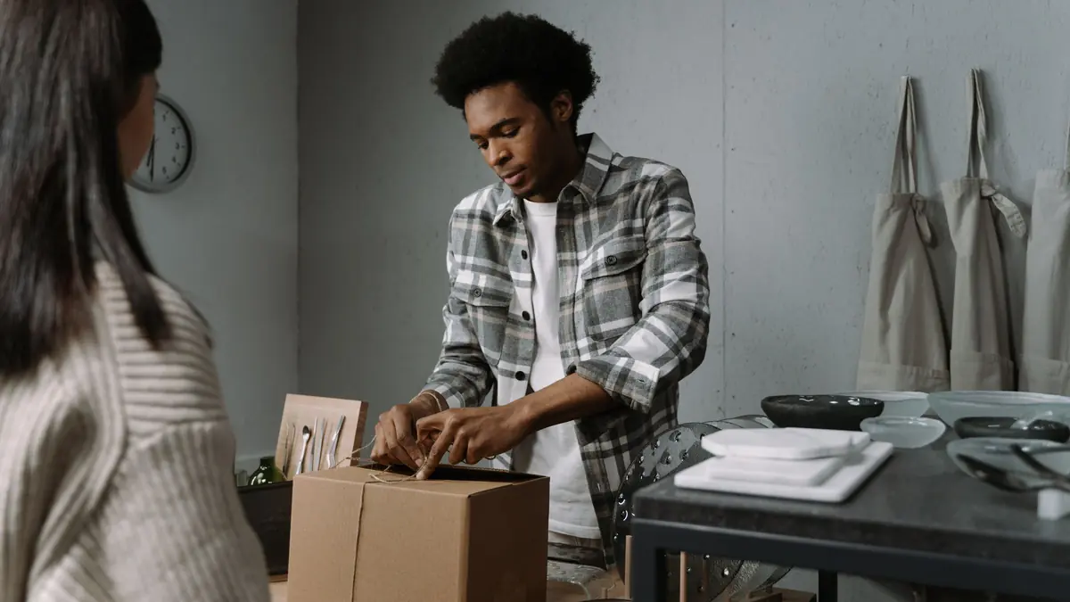 A shopkeeper ties string around a cardboard box on the counter while a customer waits