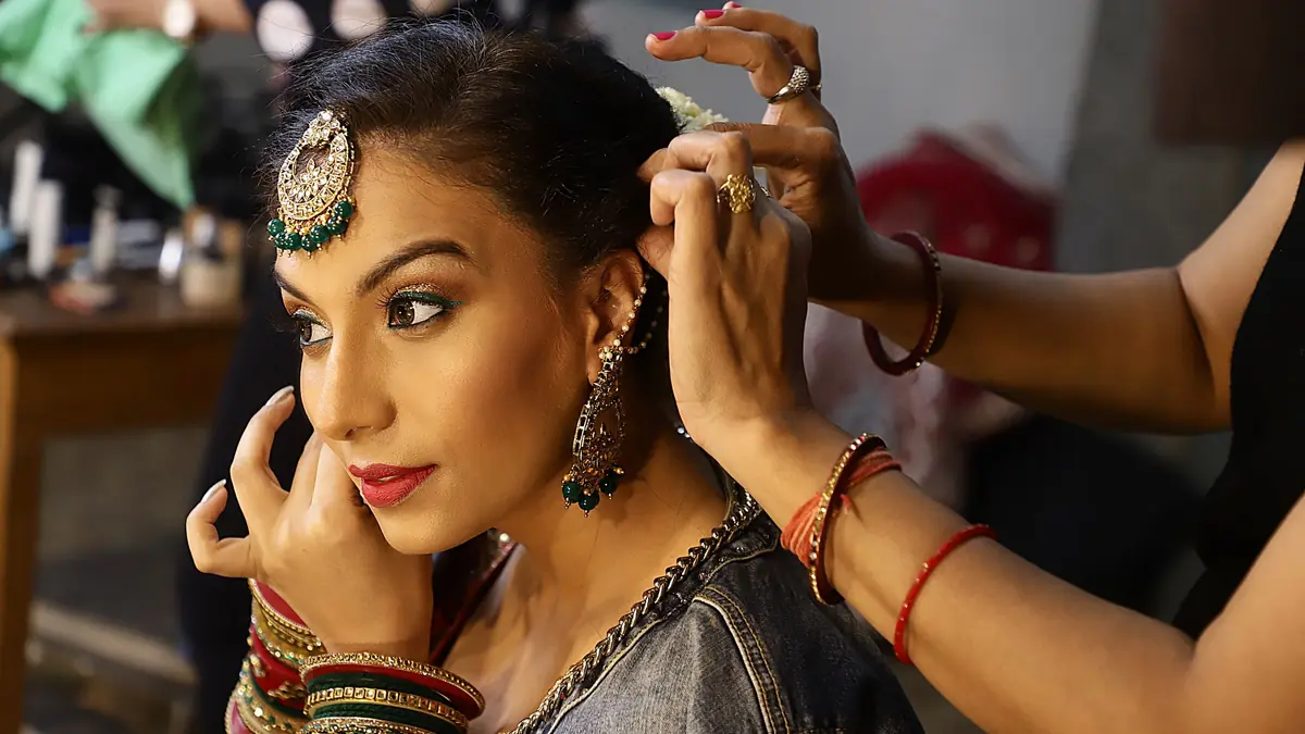 A stylist arranges the hair and maang tikka of a woman in bridal jewellery as she gets ready in a salon