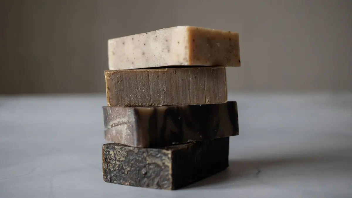 Four bars of handmade soap in shades of cream and brown stacked on a grey stone surface