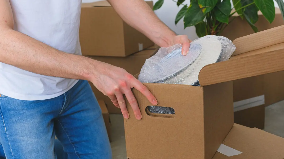 A man places bubble-wrapped plates into a cardboard box