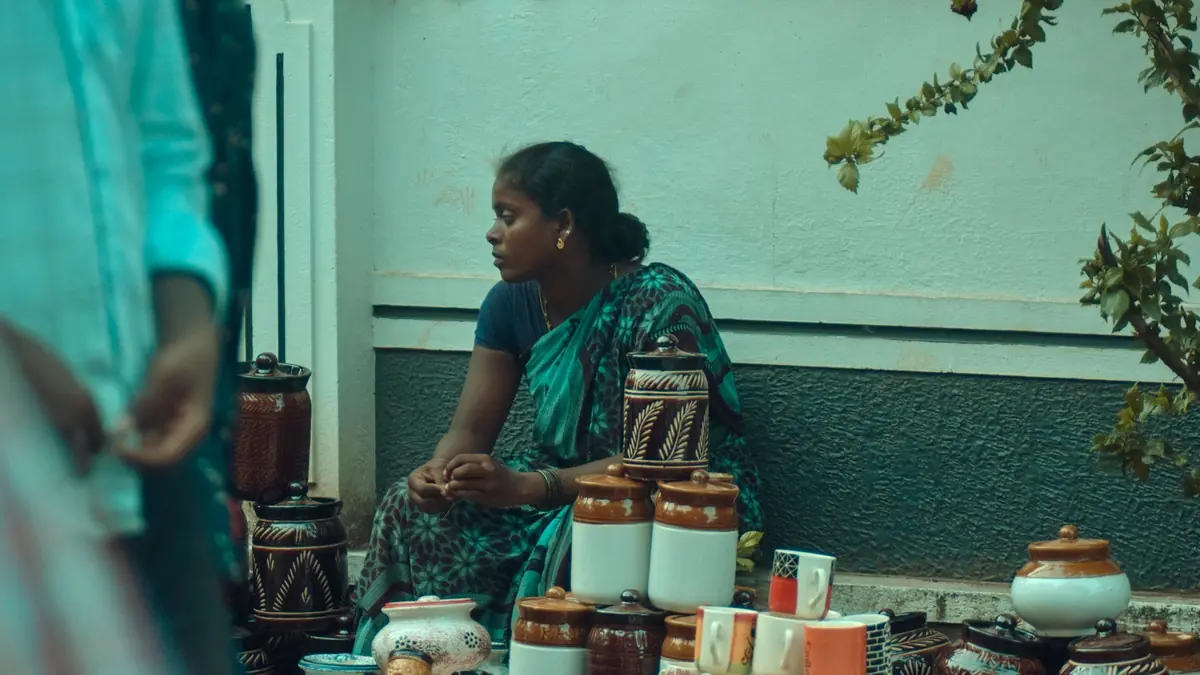 A woman in a green sari sits beside her stall of handmade clay pots, jars and mugs at an outdoor market
