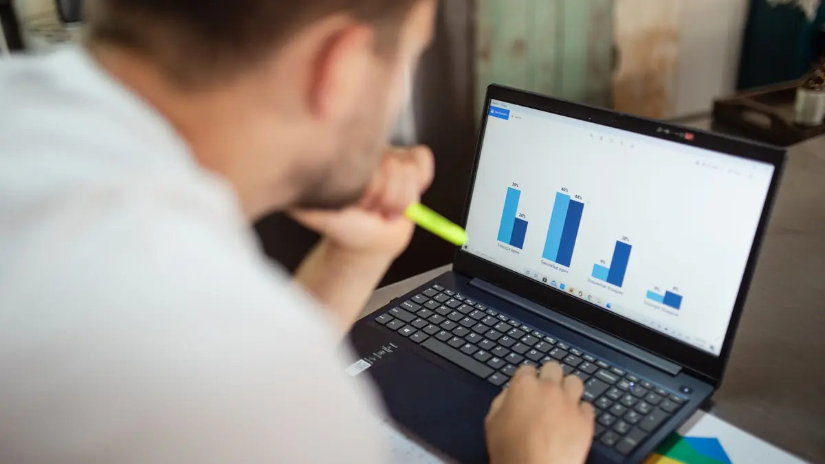 A man, seen over his shoulder, studies a simple bar chart on his laptop