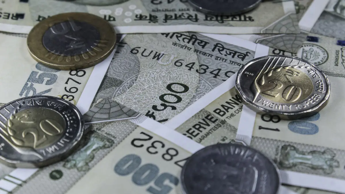 Indian rupee banknotes with ten- and twenty-rupee coins scattered on top