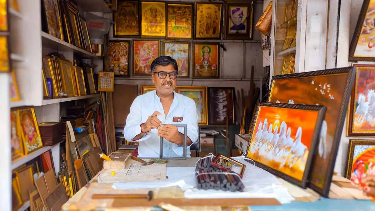A smiling shop owner sits at his counter in a picture-framing shop in Jodhpur, surrounded by framed artwork