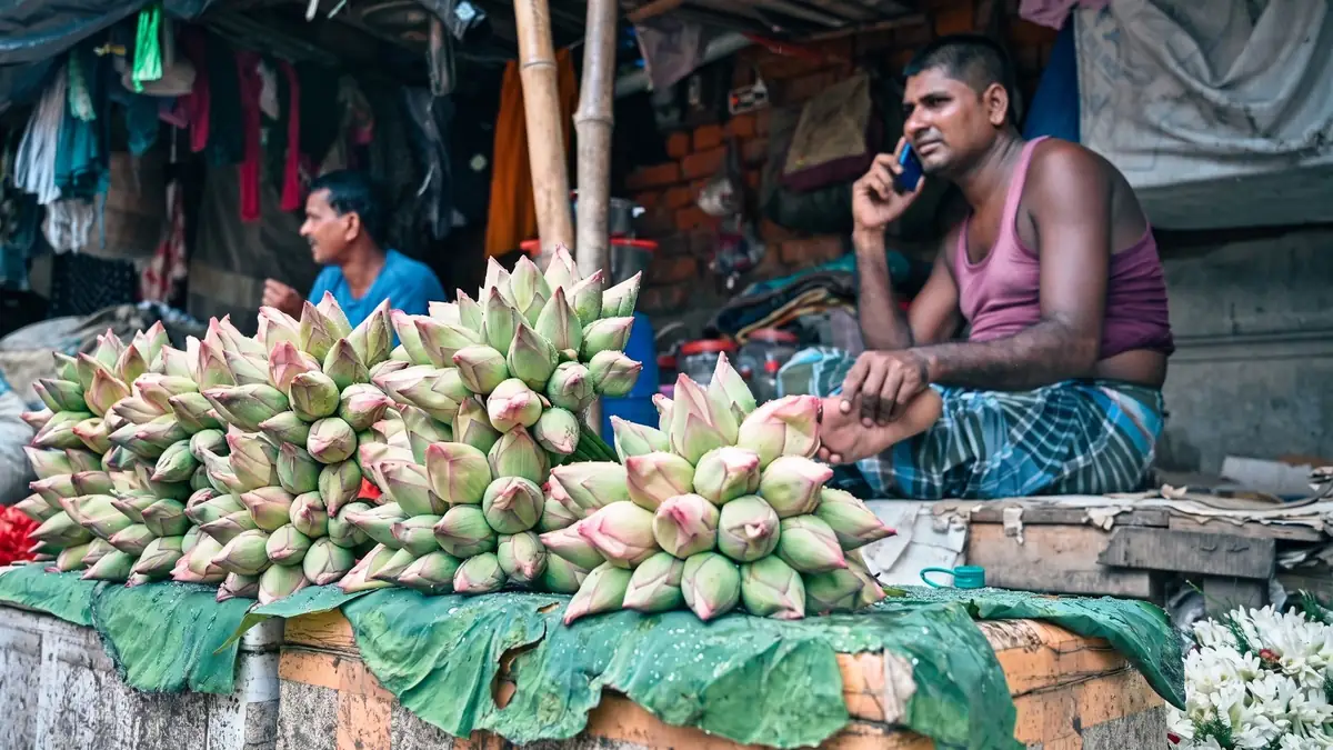 A flower seller talks on his phone behind a stall piled with lotus buds and white flowers